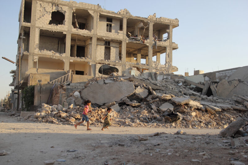 Två små barn springer bland ruinerna i Syrien.