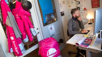 Anders Teglund sitter vid sitt skrivbord, bredvid honom hänger kläder från Foodora.