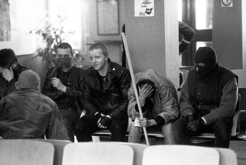 Ett gäng nazister sitter inne i Växjös stationshus. En med synligt ansikte, de andra maskerade eller med nedböjda huvuden.