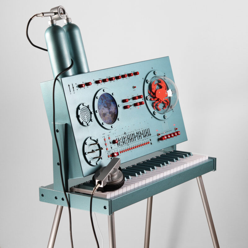 Bild på Love Hulténs konstverk med titeln Cousteau. Ett digitalpiano, polyfonisk synthesizer och röstförställande vocoder, samt videoskärm och mekanisk krabba.